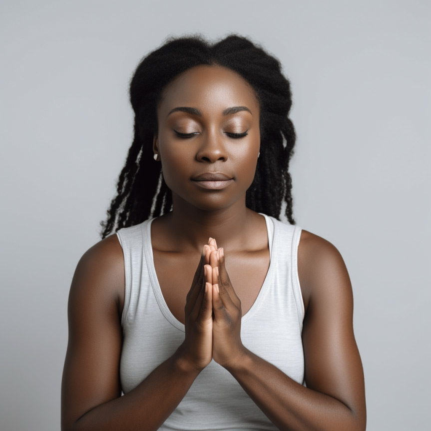 A black woman with closed eyes sits in a yoga pose, hands together in a prayer position.